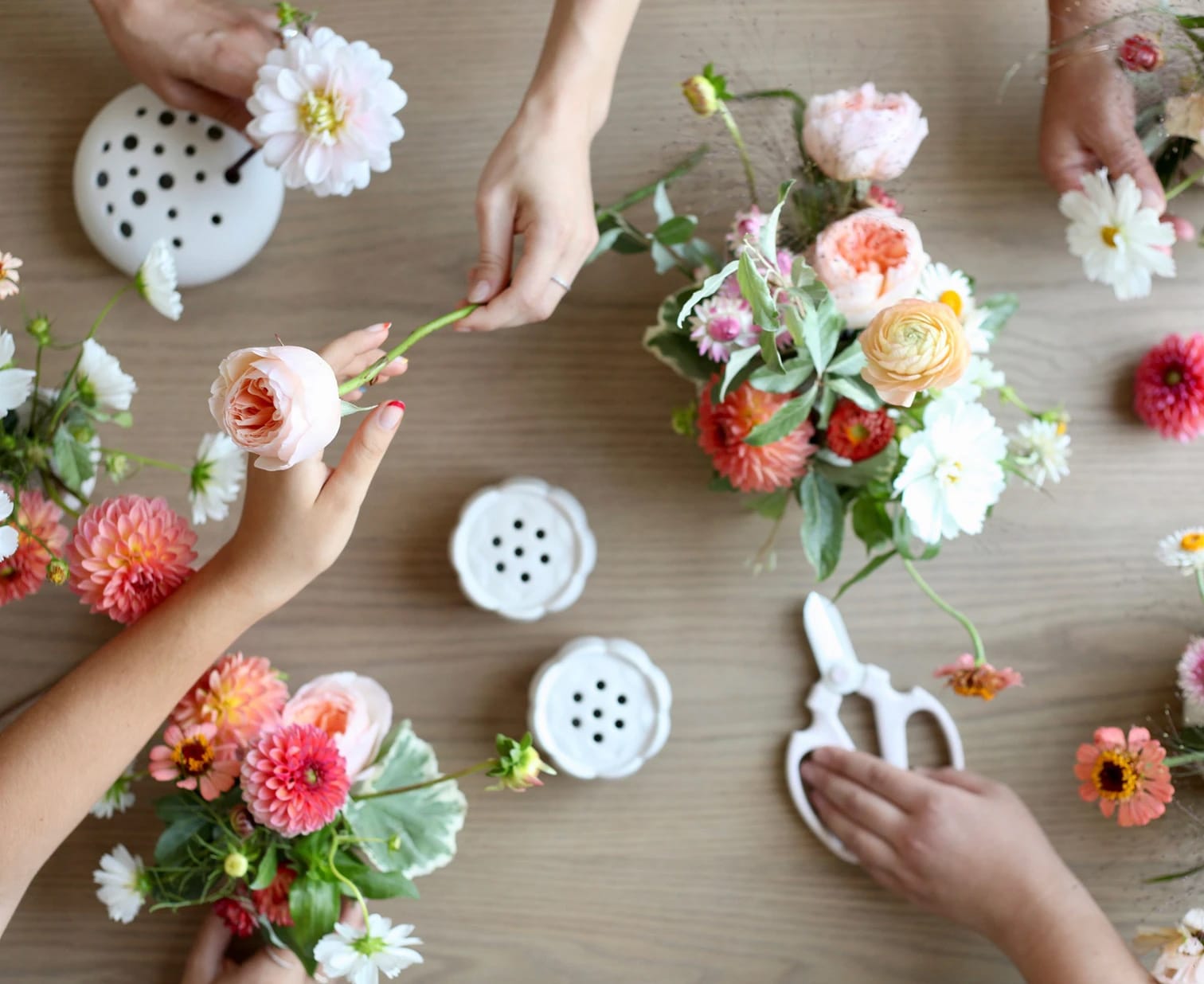 Hands arranging fresh-cut flowers at a Floral Society workshop table