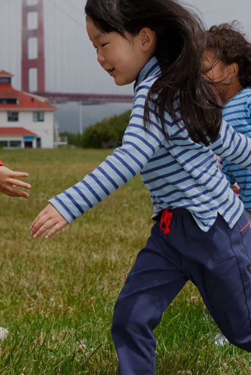 Two children in striped Oso & Me tops playing on grass near the Golden Gate Bridge